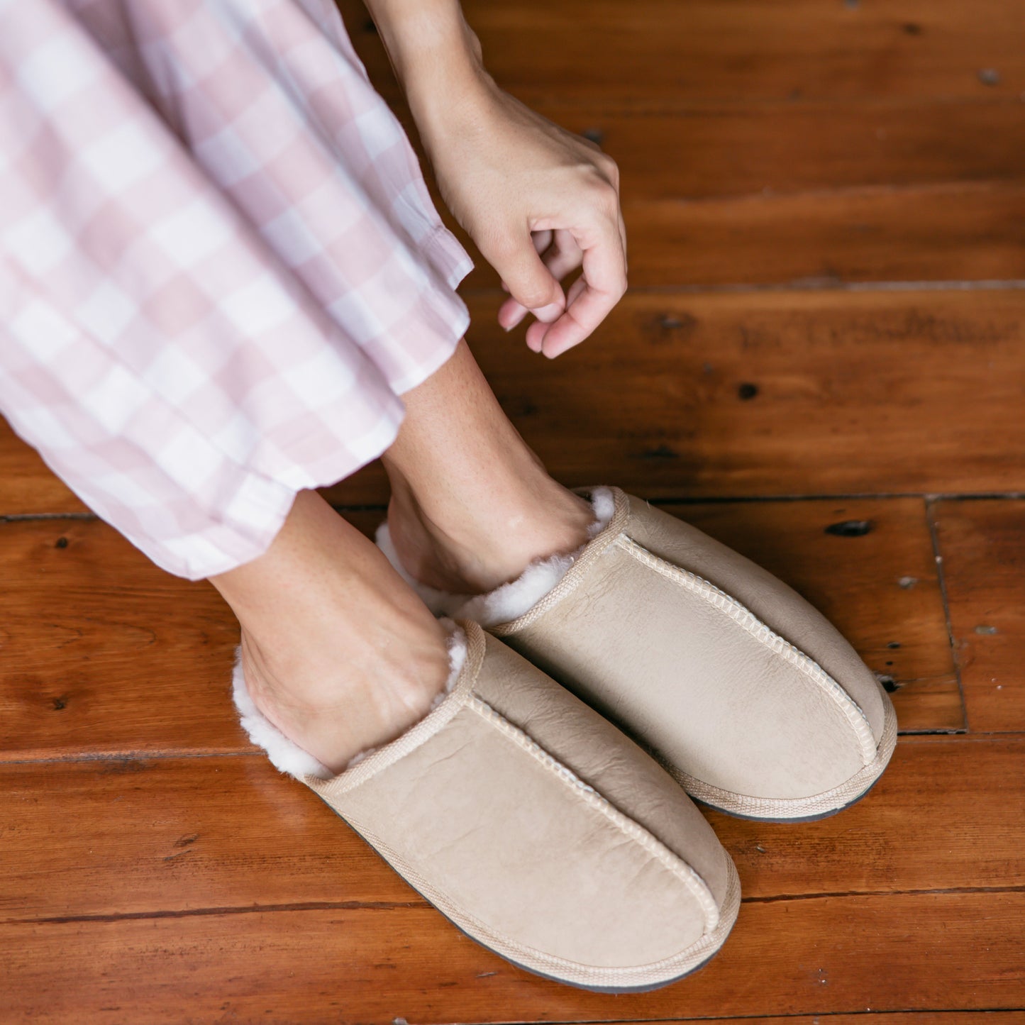 Person wearing beige slippers on a wooden floor
