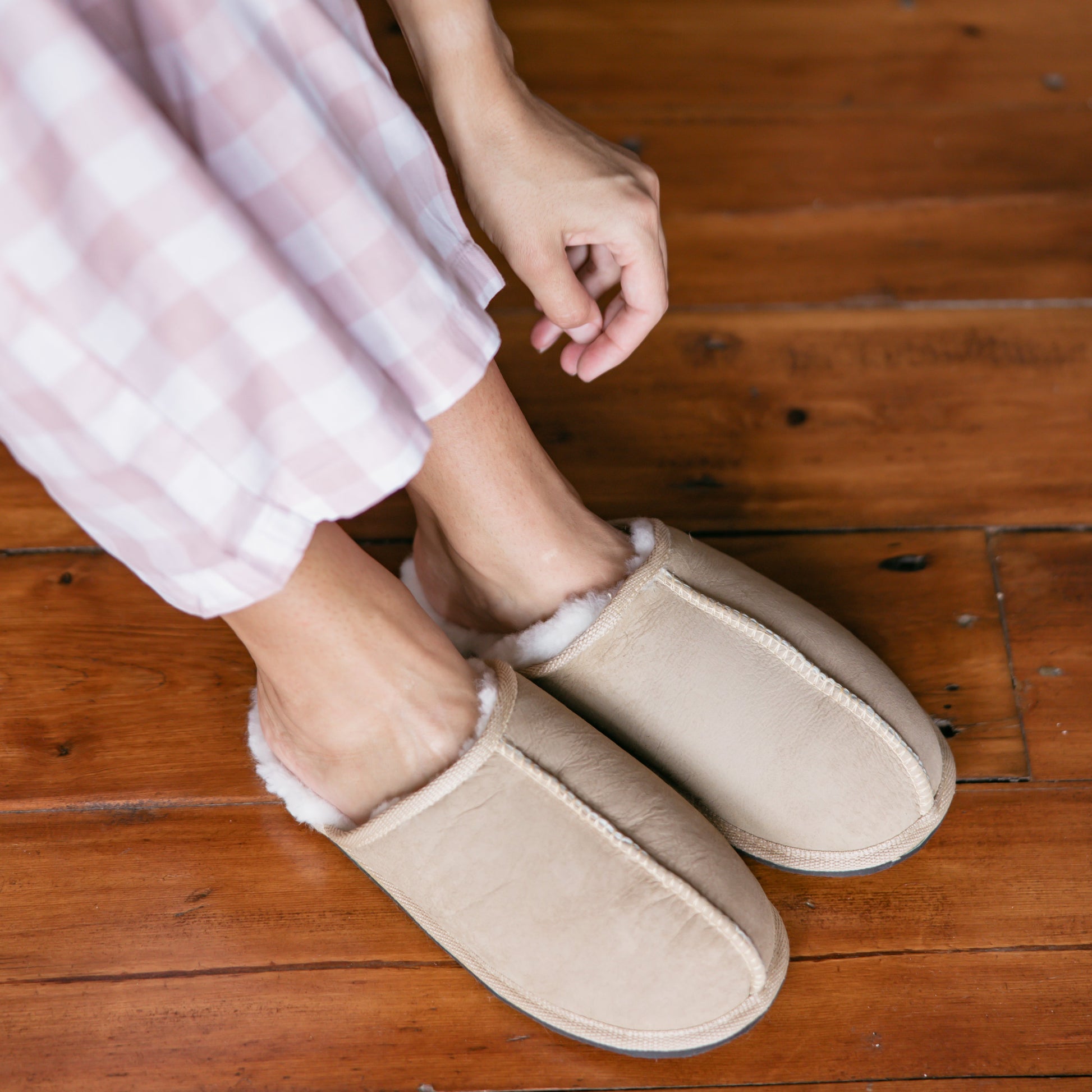 Person wearing beige slippers on a wooden floor
