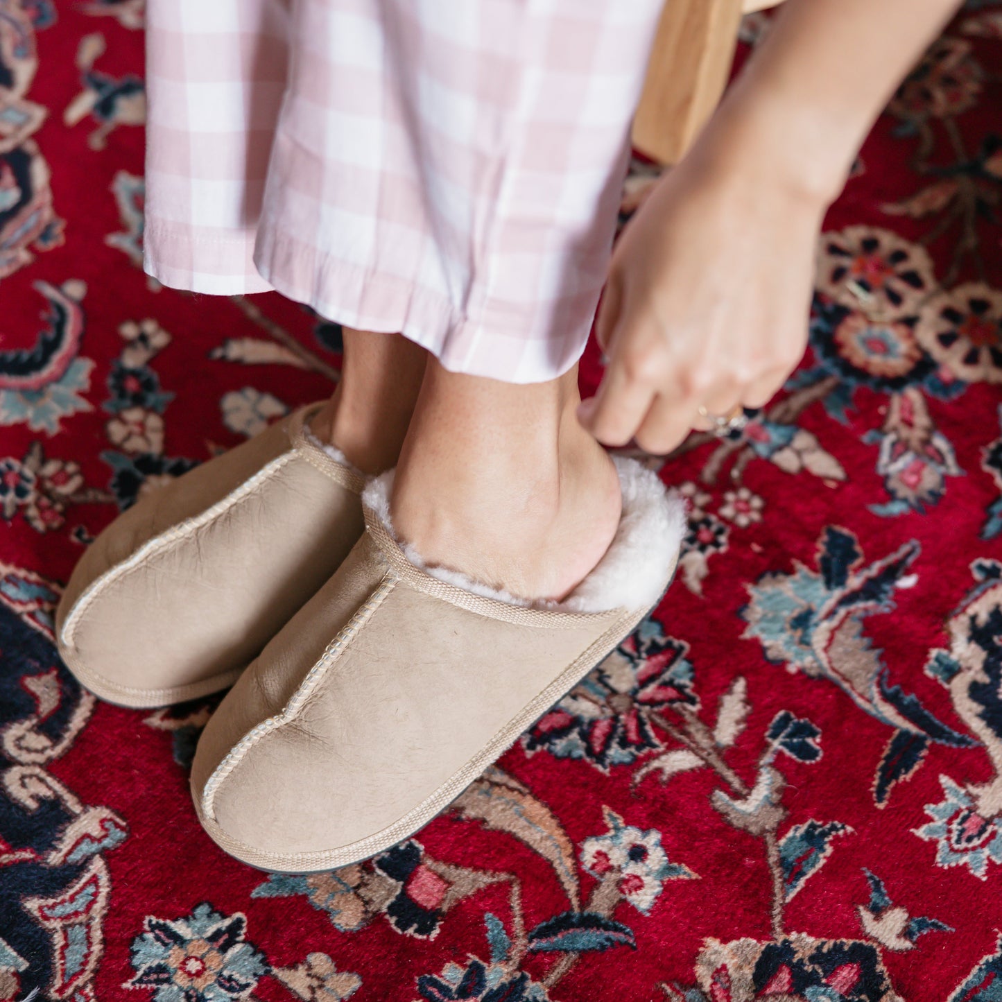 Person wearing beige slippers on a red patterned rug