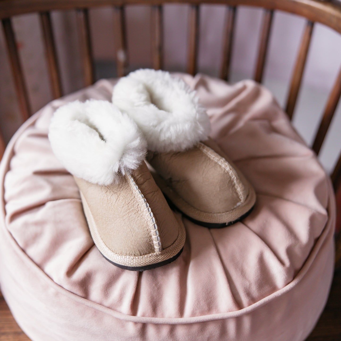 Pair of beige slippers with white fur trim on a pink cushion.