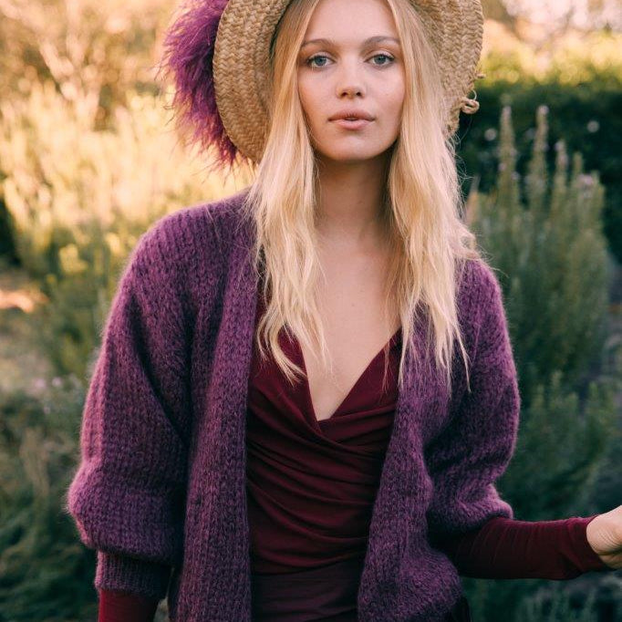 Woman wearing a purple mohair cardigan and maroon dress with a straw hat in a garden setting