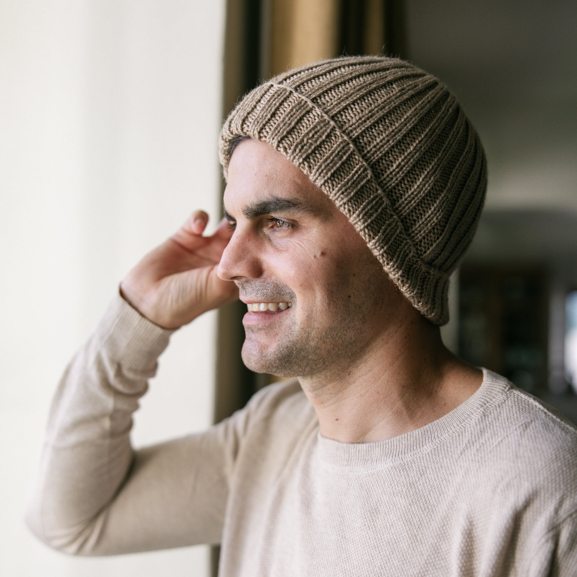 Man wearing a beige knit beanie and light gray sweater indoors.