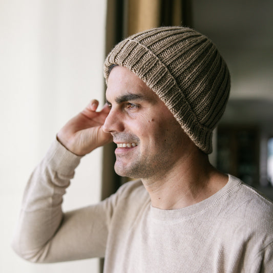 Man wearing a beige knit beanie and light gray sweater indoors.